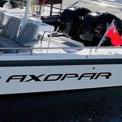 White boat with 'Axopar' branding on a dock with other boats in the background.