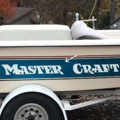 White boat with 'Master Craft' branding on a trailer, surrounded by trees and foliage.